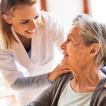Lächelnde Pflegerin spricht mit alter Frau und greift an ihre Schulter in Graz